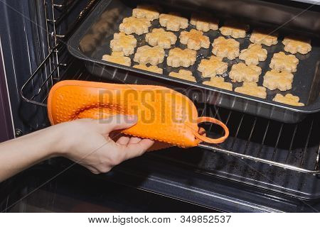 Taking Fresh Baked Four-leaf Clover Shaped Cookies Out Of Oven With Orange Silicone Potholder