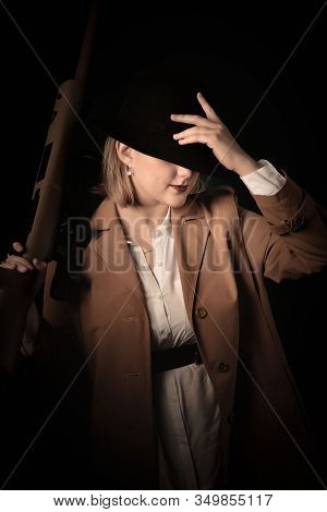 Retro Gangster Woman In A Brown Cloak And Black Hat With Airguns In Hands. Photoshoot In The Style O