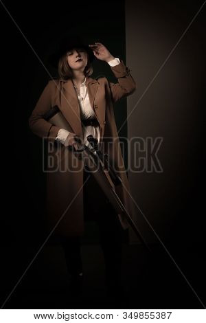 Retro Gangster Woman In A Brown Cloak And Black Hat With Airguns In Hands. Photoshoot In The Style O