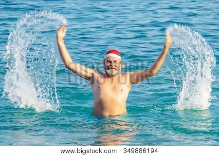 Adult Charismatic Smiling Bearded Man In A Santa Hat Is Swimming In The Sea, Vacation Of An Adult Ch