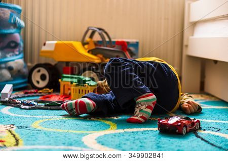 Poznan, Poland - January 19, 2020: Young Boy Laying On A Carpet Floor Playing With A Plastic Train S