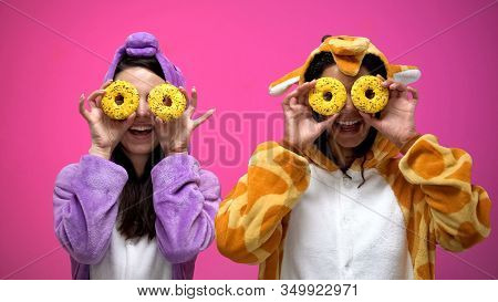 Young Women In Funny Pajamas Closing Eyes With Donuts, Fooling Around, Joke