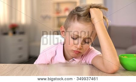 Sad Boy Sitting At Kitchen Table, Refusing To Eat Healthy But Tasteless Meal