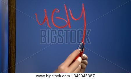 Female Hand With Red Lipstick Writing Word Ugly On Mirror Surface, Problem