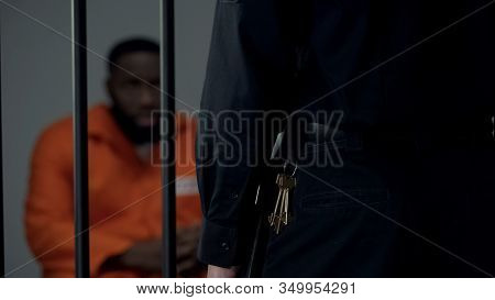 Security Warden With Keys Looking At Afro-american Imprisoned Male In Cell