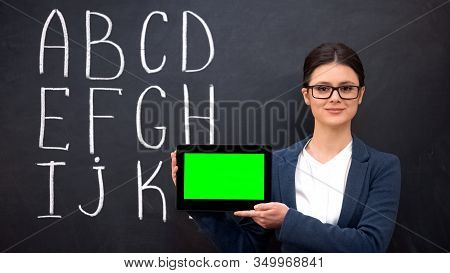 Smiling Teacher Holding Prekeyed Tablet, Alphabet On Blackboard, Innovations