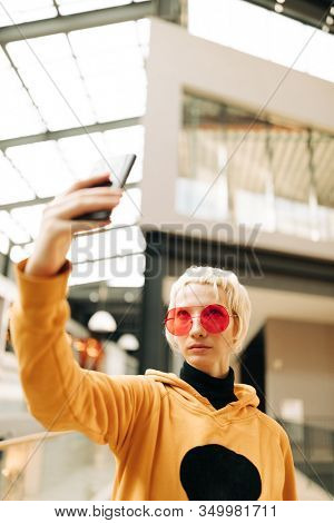blond lesbian woman with red singlasses and cellphone