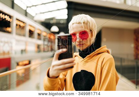 blond lesbian woman with red singlasses and cellphone