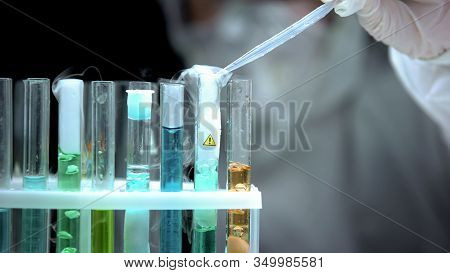 Researcher Pouring Liquid To Sample Boiling In Test Tube With Warning Symbol