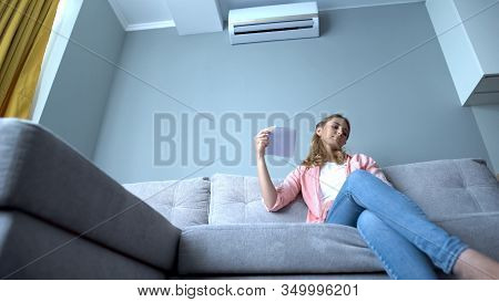 Woman Waving Paper Sitting On Couch, Suffering Heat, Faulty Air Conditioning