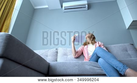 Woman Looking At Broken Air Conditioner Sitting On Couch, Suffering Heat