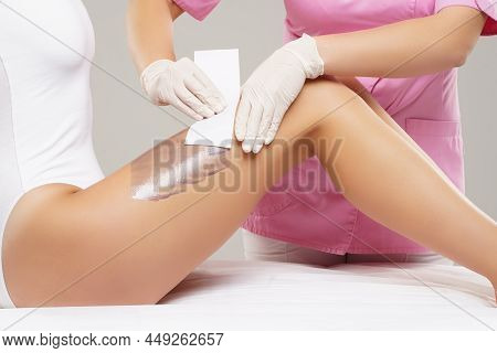 Beautician Is Removing Hair From Young Female Body And Legs With Hot Wax. Woman Has A Beauty Treamen