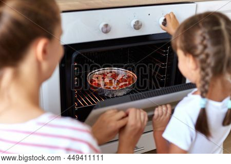 Back View Of Mum And Kid Daughter Bake Muffins In Kitchen, Mother Teaching Child Take Tray With Cupc