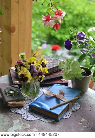 Summer Still Life With Old Decorated Book, Crystal Stines And Beautiful Flowers In Pots Outside In T