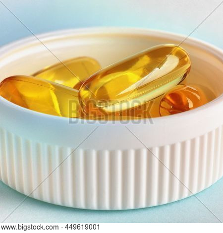 Yellow Softgels Or Capsules Are In Bottle Cap. Fish Oil. White And Blue Surface. Vitamins And Health