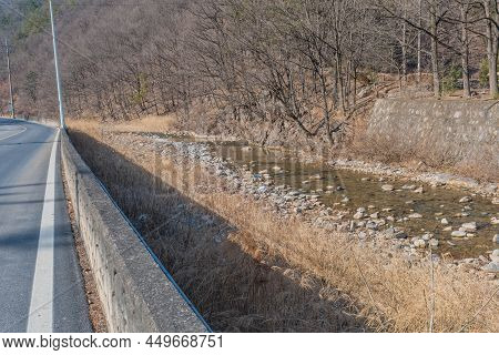 Stream Flowing Beside Country Road In Woodland Mountain Countryside.