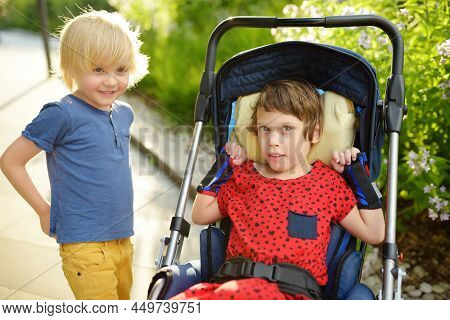 Little Boy And Disabled Girl In Wheelchair Playing Together In A Summer Park. Child Cerebral Palsy. 