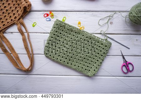 Knitted Bag Of Green Color In The Process Of Knitting, A Skein Of Green Yarn, A Hook. Markers, Sciss