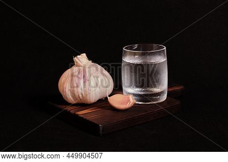 Still Life On A Dark Background. A Glass Of Vodka And Garlic On A Wooden Stand