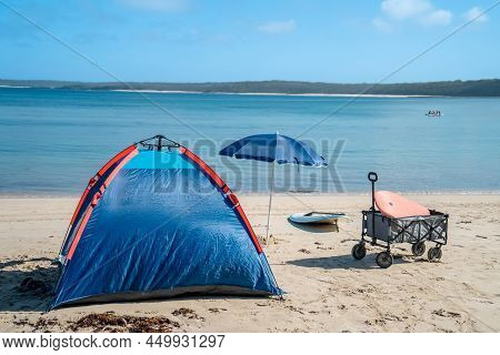 Outdoor Beach Cart Wagon And Beach Umbrella On A Sandy Beach Near The Ocean. Family Vacation Holiday