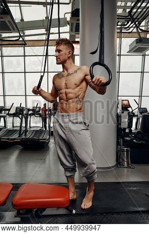 Strong Man Doing Exercise On To Gymnastic Rings At Gym. Fit Male Athlete Training On Gymnastic Rings