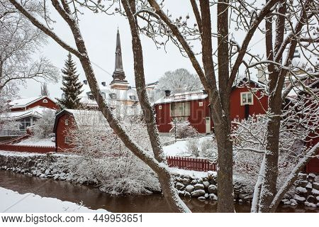 White winter in Sweden, Swedish style traditional red houses, pointed spire of cathedral, Idyllic nordic cityscape Vasteras old town in snow at Svartan Black river