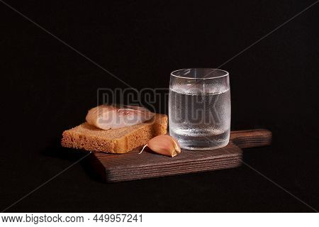 Still Life On A Dark Background. A Glass Of Vodka, A Sandwich With Rye Bread And Herring, Garlic On 
