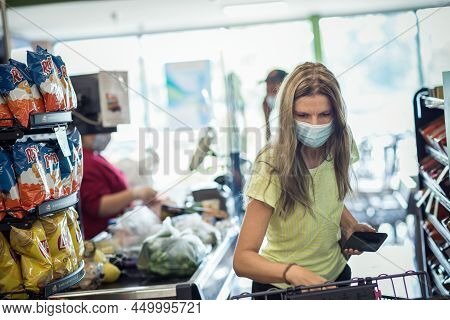 Chicago, Il- August 21, 2021 A Woman With Face Mask Loading Groceries Onto The Checkout Conveyor Bel