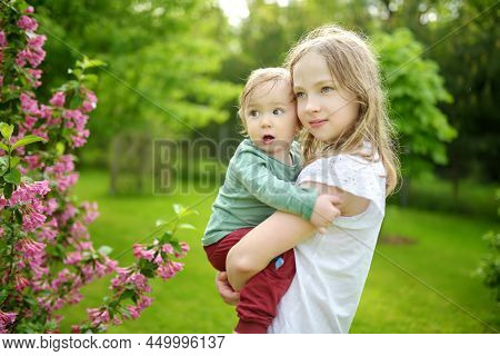 Big Sister And Her Toddler Brother Having Fun Outdoors. Young Girl Playing With Baby Boy On Spring D