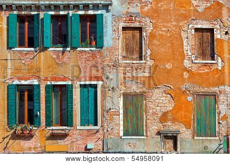 Facade of typical old colorful house with small windows, wooden shutters and cracked brick wall in Venice, Italy.