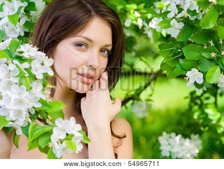 Portrait of young woman touches her face standing near the flowered tree in the park. Concept of youth and natural beauty