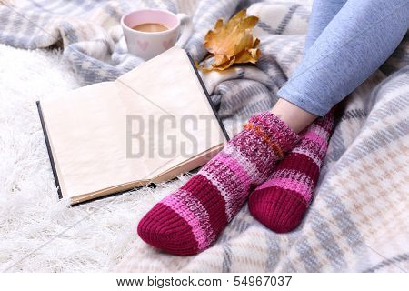 Composition with warm plaid, book, cup of hot drink and female legs, on color carpet background