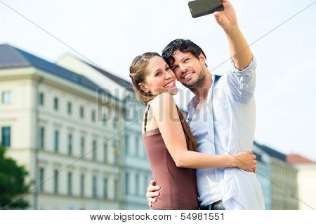 Man and woman or young couple making trip as tourists in Munich and making snapshot with the smartphone or phone