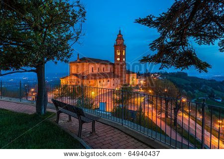 Bench on walkway and view of illuminated church on background in the morning in Piedmont, Northern Italy.