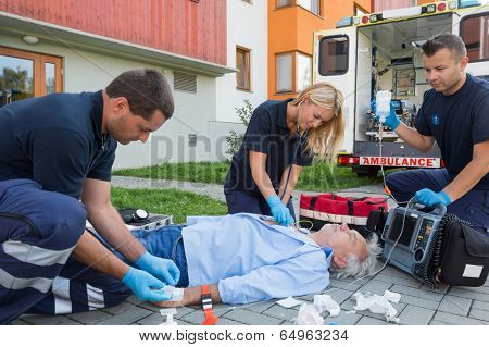 Paramedics giving firstaid to unconscious senior patient lying on ground