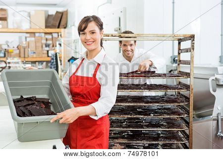 Portrait of beautiful female worker showing beef jerky in basket with colleague standing in background