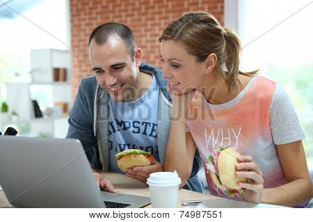 Roommates eating sandwich in front of laptop