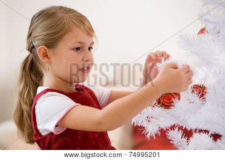 Little girl decorating white christmastree