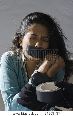 Kidnapper's hands wrapping adhesive tape around an abducted young woman's hands