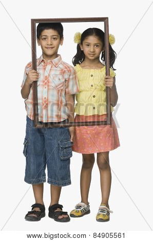 Portrait of a girl and a boy holding an empty picture frame