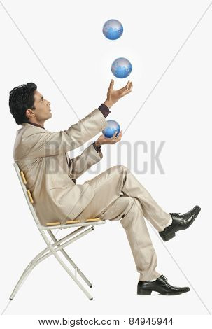 Businessman sitting on a chair and juggling with globes