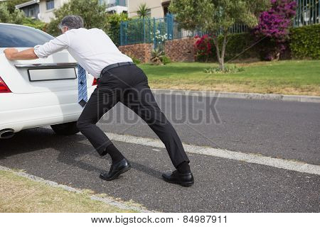 Man pushing his broken down car on the road