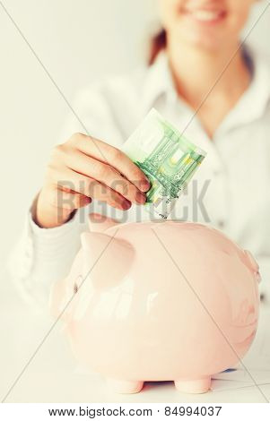 business, office, household, school, tax and education concept - woman puts euro cash into large piggy bank