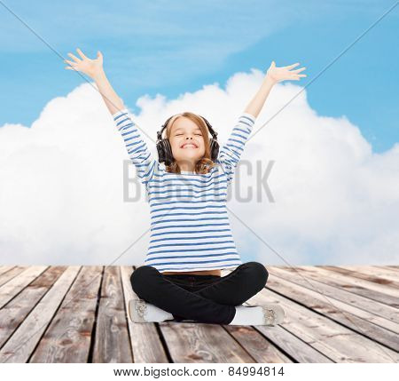 music, childhood, people and technology concept - happy girl with headphones listening to music over blue sky and cloud background