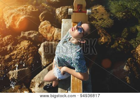 Attractive woman posing with her skateboard in front of the sea while enjoying summer sunshine