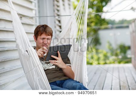 Young Man Relaxing In Hammock  And Using Tablet Computer