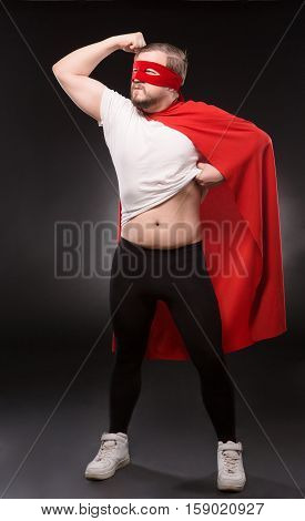 Handsome man with red mask on in super hero costume. Super hero man showing his strong body isolated on black background. Super hero man ready to help world.