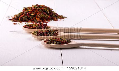 three wooden spoons with dried peppers and seeds (chili peppers habanero jalapeno rawit birds eye chili thai chili) on a white wooden place.