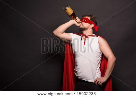 Super anti hero man drinking alcohol while posing in studio. Handsome man drinking alcohol drinks while posing for photogrpher.
