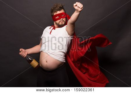 Bad super hero man in red mask holding bottle with wine or whiskey in studio. Handsome man with raised wrist isolated on black background in studio.
